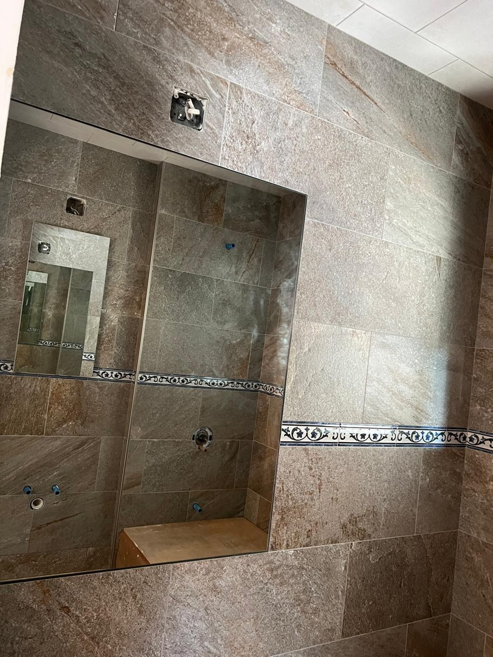 Finished stone tile bathroom wall with decorative border and mirror